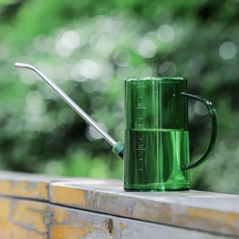 Green watering can with a long spout on a wooden surface with a blurred green background