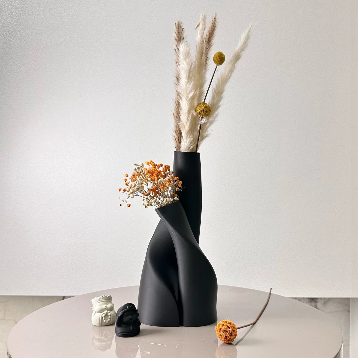 Black abstract vase with dried flowers on a white surface