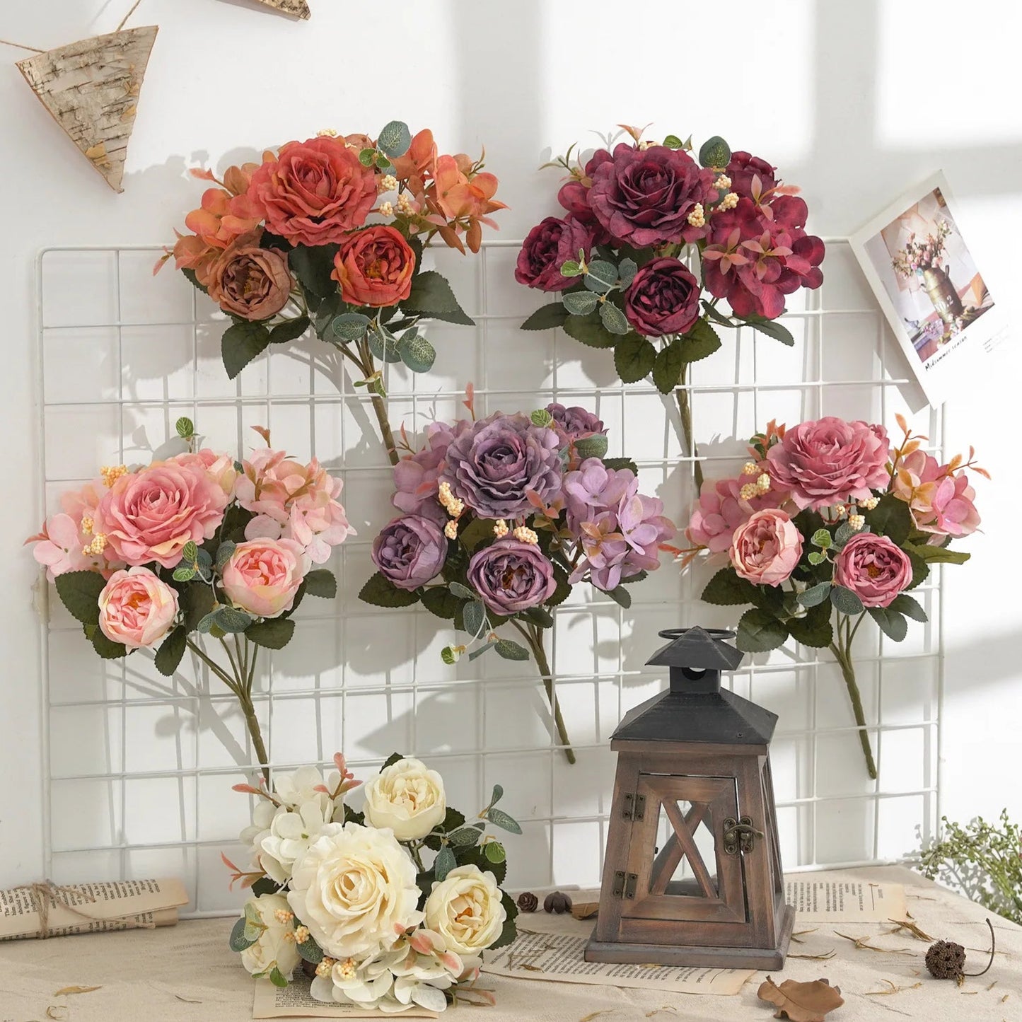 Set of artificial flower bouquets in various colors on a decorative surface with a lantern.