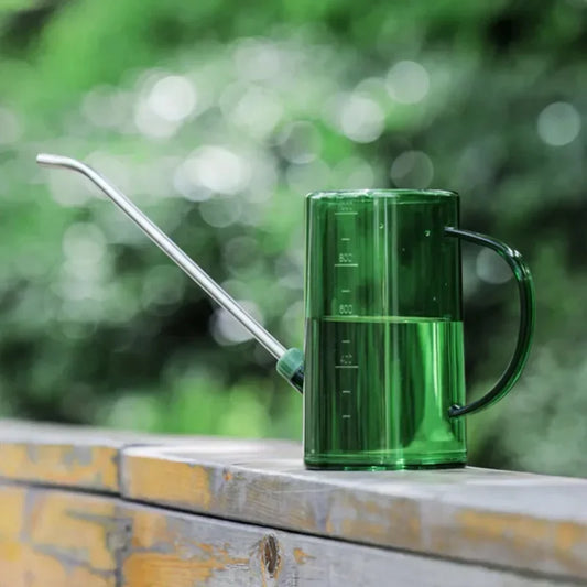 Green watering can with a long spout on a wooden surface with a blurred green background