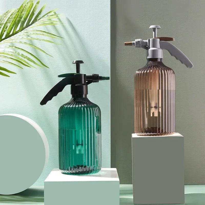 Glass spray bottle and white vase with plant on a wooden table against a gray wall.