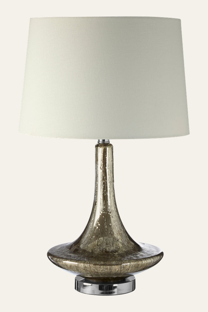 Amayana Glass Table Lamp with seeded amber-tinted glass flared base and slender neck on a chrome round pedestal, topped with a white fabric drum shade.