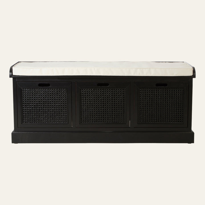 Arlen Bench — rectangular black wood storage bench with three woven cane front panels, recessed finger‑hole handles, and a cream seat cushion