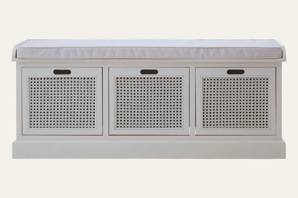Arlen Bench — white painted wood storage bench with three rattan cane-front panels, recessed cutout handles, and a light beige padded seat cushion