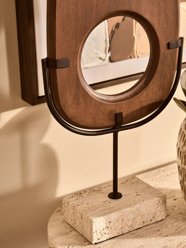 Arsen Wood Vertical Sculpture — warm brown wooden oval panel with round center cutout, mounted in a matte black U-shaped metal frame and slender rod on a light textured stone base.