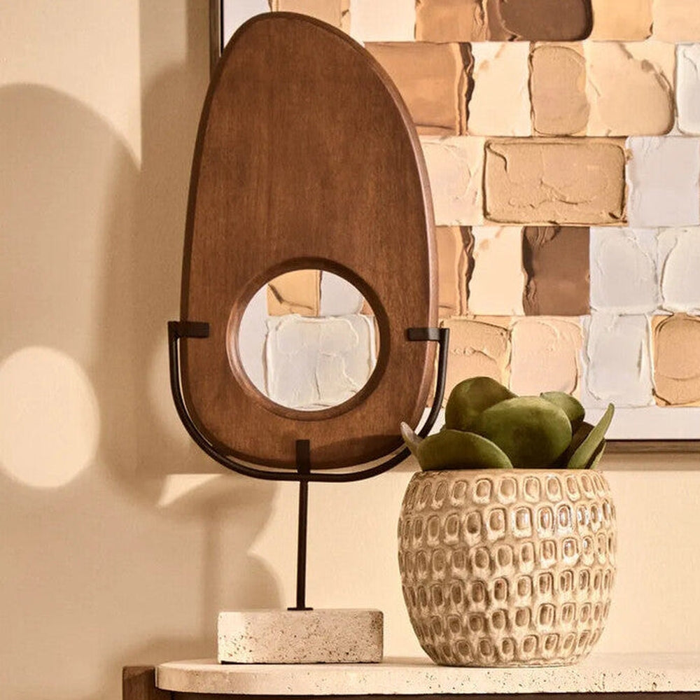 Arsen Wood Vertical Sculpture — oval teardrop wooden sculpture with round center cutout, warm stained wood finish mounted on black metal stand with rectangular stone base, displayed on a tabletop.