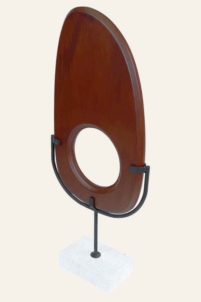 Arsen Wood Vertical Sculpture: tall oval warm-brown stained wood panel with central round cutout, mounted in a black metal U-frame on a rectangular white stone base.