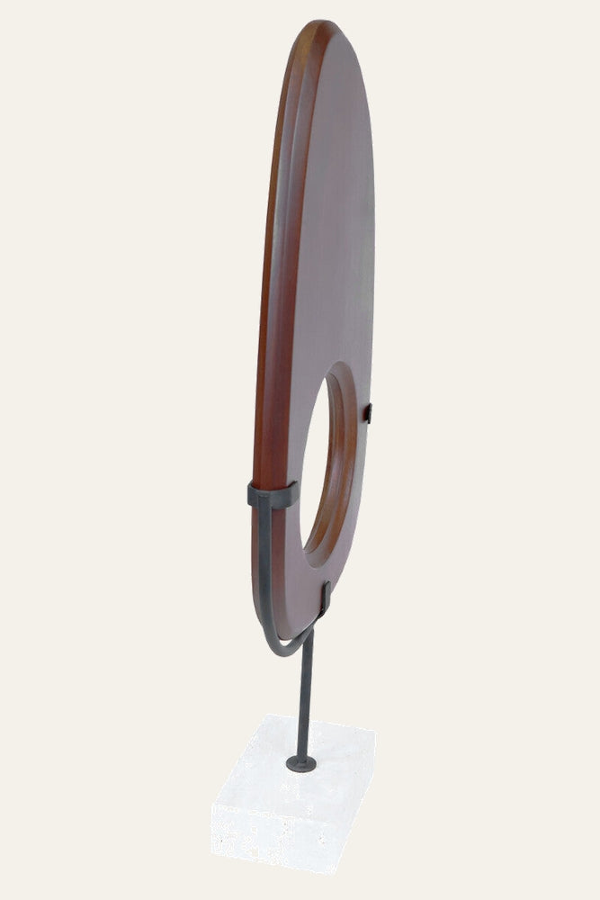 Arsen Wood Vertical Sculpture: dark-stained vertical wood oval with circular center cutout, black metal brackets and slim rod on a white stone base
