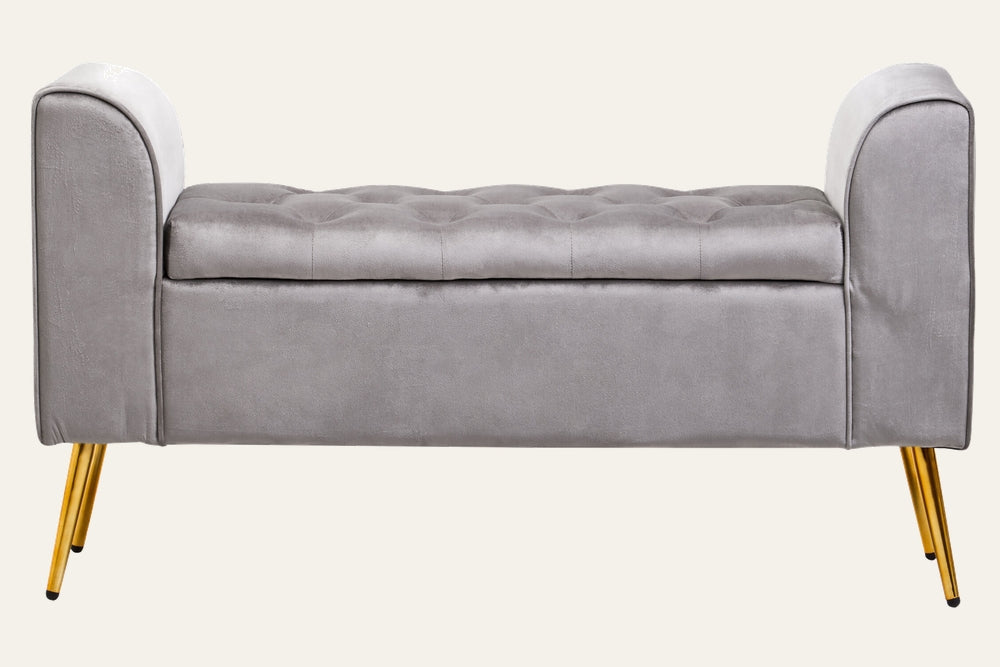 Caelis Velvet Storage Bench in light gray velvet with tufted top, low curved armrests and gold tapered metal legs.