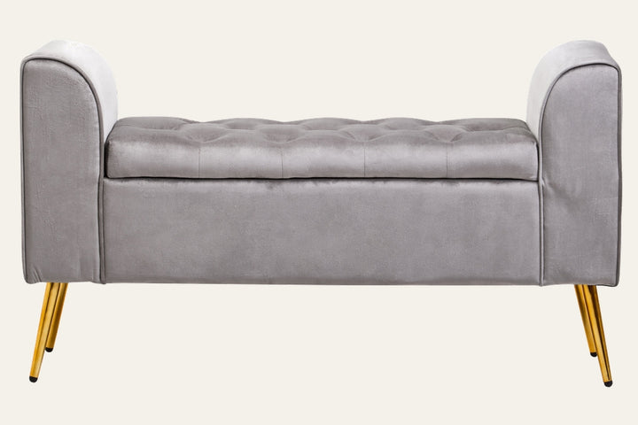 Caelis Velvet Storage Bench in light gray velvet with tufted top, low curved armrests and gold tapered metal legs.