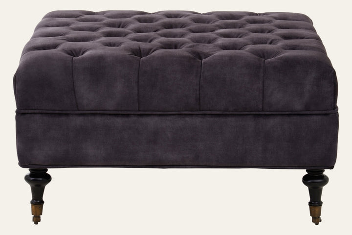 Caia Grey Velvet Ottoman - square tufted grey velvet ottoman with piped edge, turned dark wood legs and brass casters