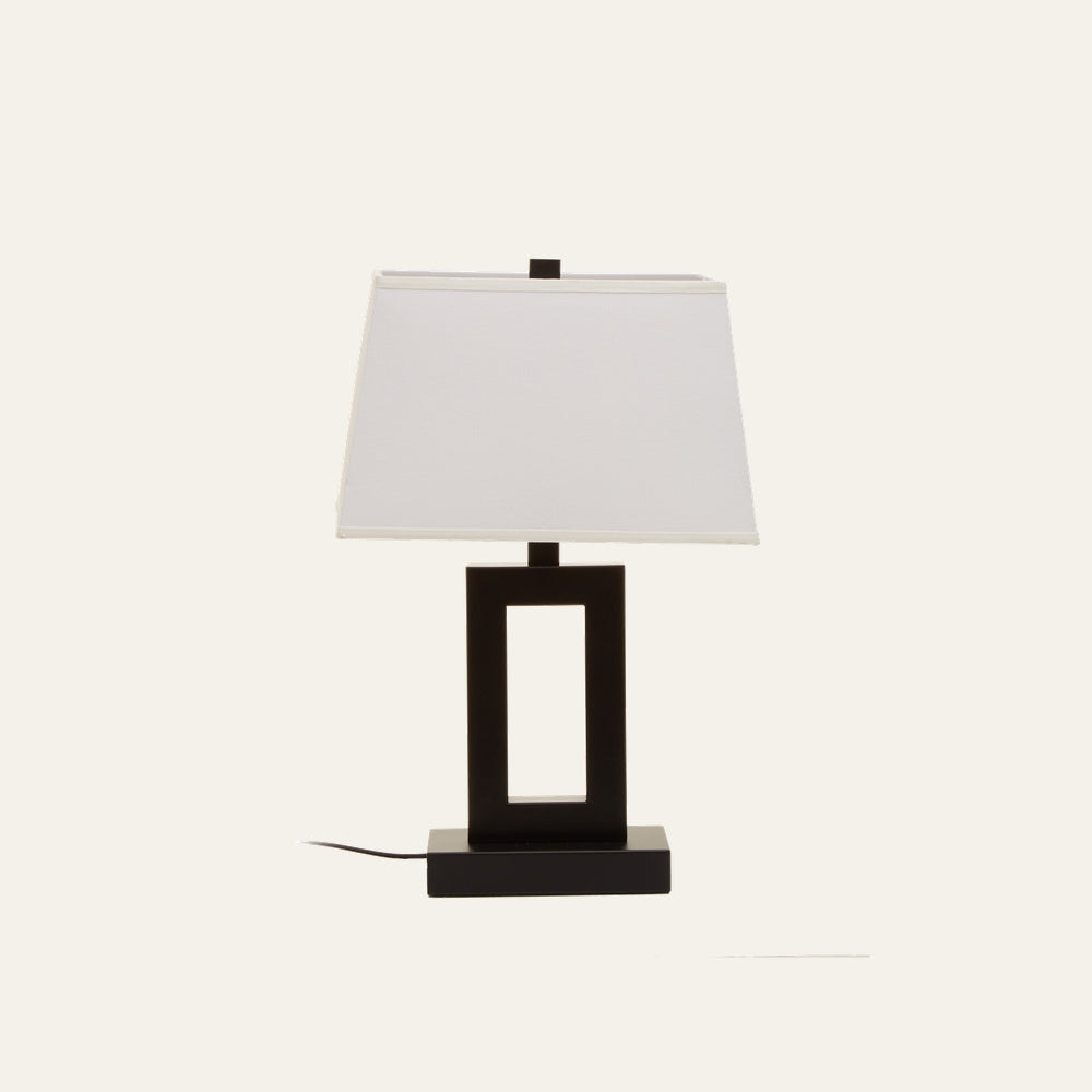 Celdora Fabric Table Lamp with white rectangular fabric shade and black open-rectangular base on a matching rectangular platform, power cord visible.