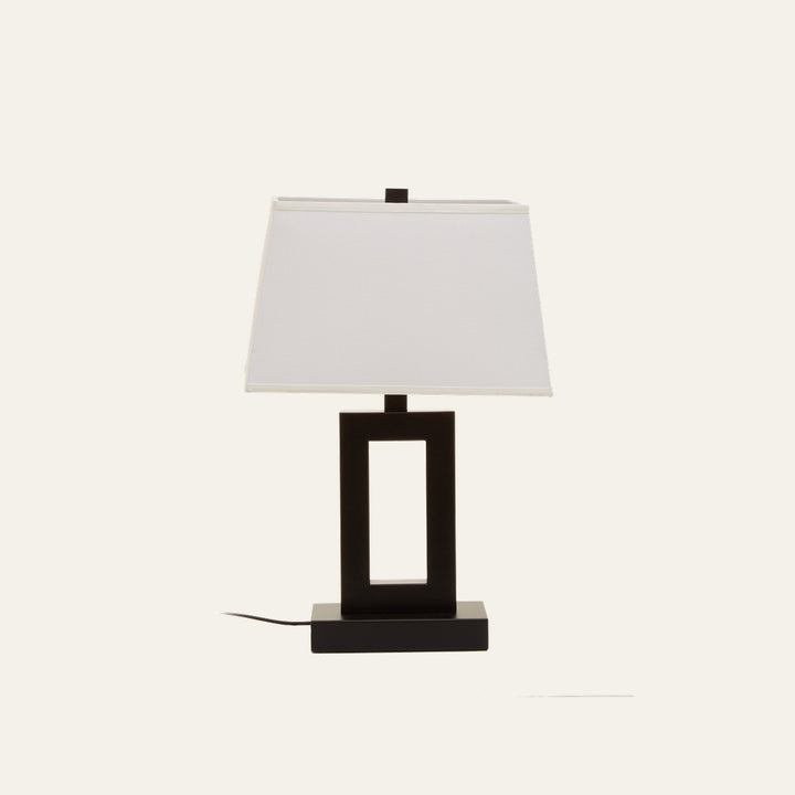Celdora Fabric Table Lamp with white rectangular fabric shade and black open-rectangular base on a matching rectangular platform, power cord visible.