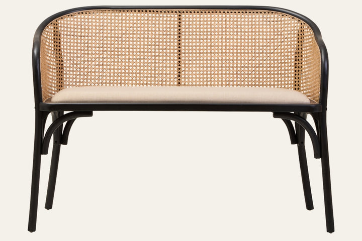 Drevan Cane Wood Bench with rounded black wood frame, natural woven cane backrest and beige upholstered seat cushion on slim black legs.