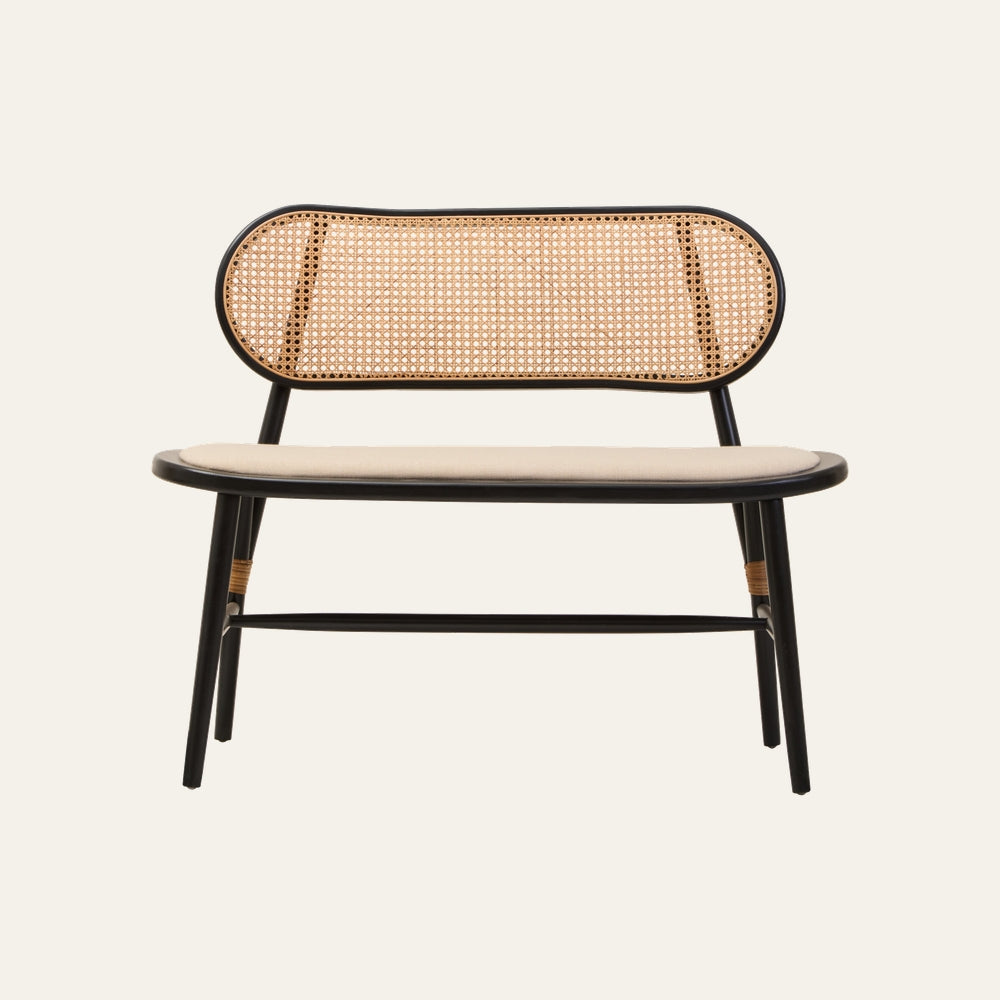 Drevan Natural Cane Black Wood Bench with oval natural cane woven backrest, black wood frame, rattan-wrapped leg accents and padded beige seat cushion.
