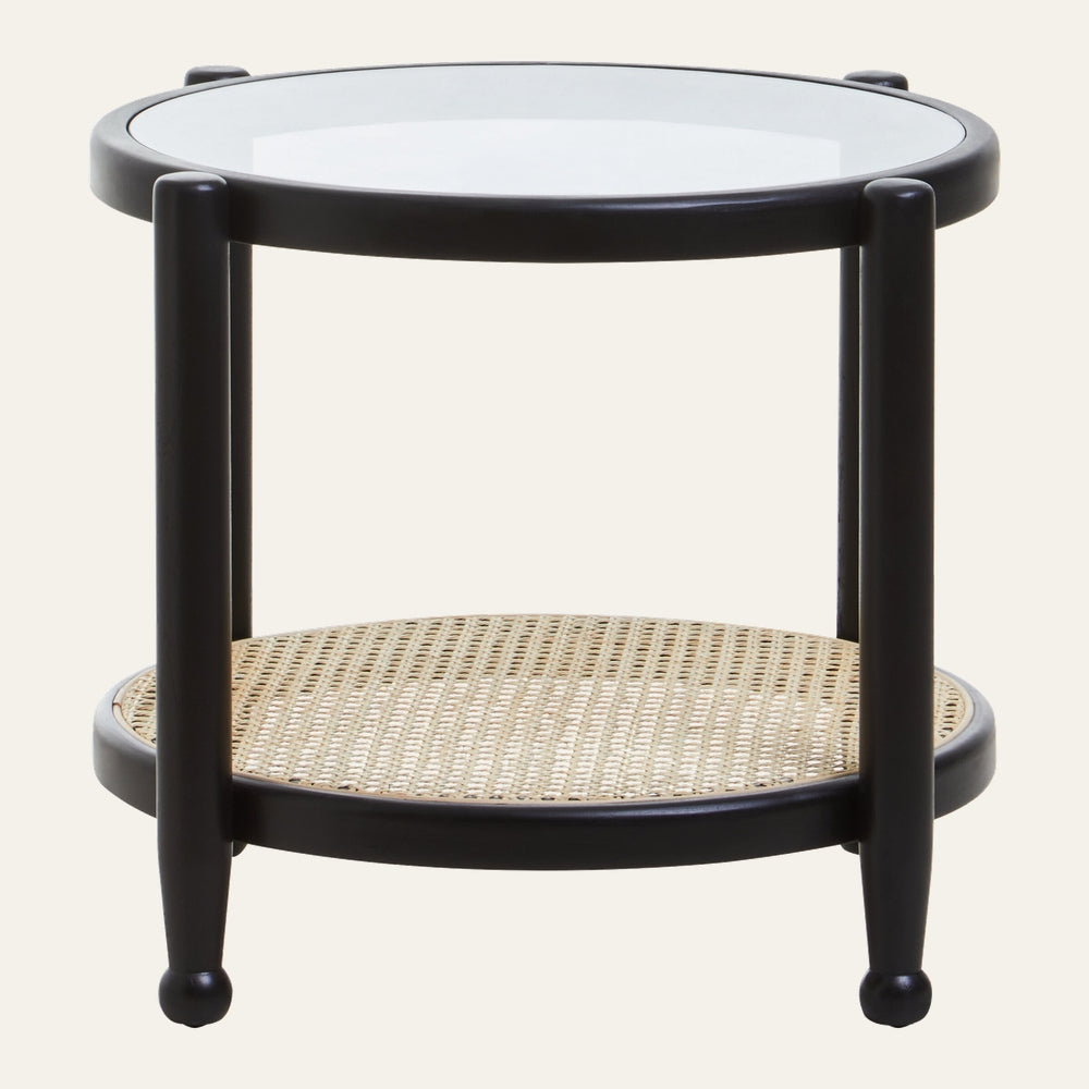 Drevan Rattan Glass Side Table — round black wood frame with clear glass top, woven natural rattan lower shelf and three tapered legs with rounded feet.