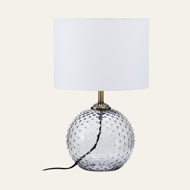Elivella Table Lamp with a white drum fabric shade, clear hobnail-pattern glass globe base, brass-tone neck, and visible black power cord