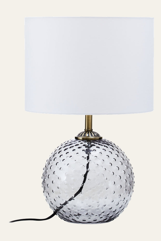 Elivella Table Lamp with white drum fabric shade, hobnail-textured clear glass orb base and brass-tone metal neck, black cord visible.