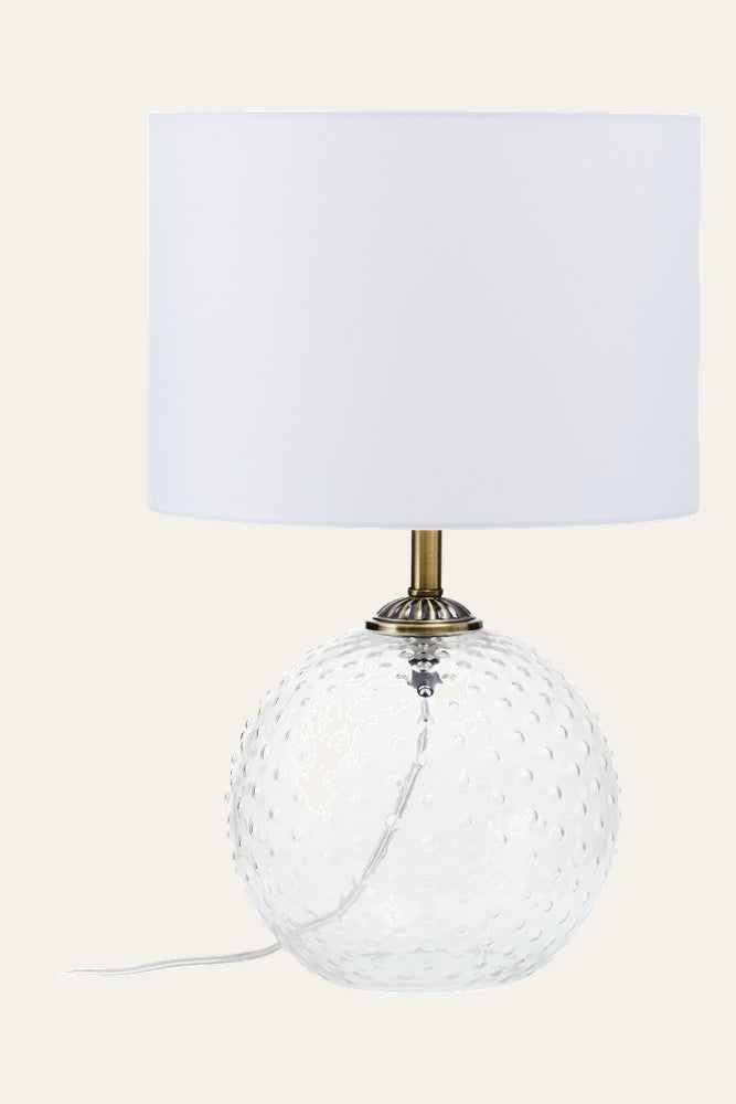 Elivella Table Lamp with clear textured glass globe base featuring raised dot pattern, brass-tone metal neck, white drum fabric shade and visible clear power cord