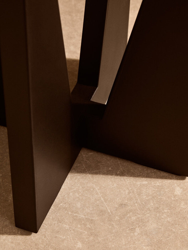 Close-up of Elsen Travertine Side Table showing angular matte dark base and beige travertine top with natural veining.