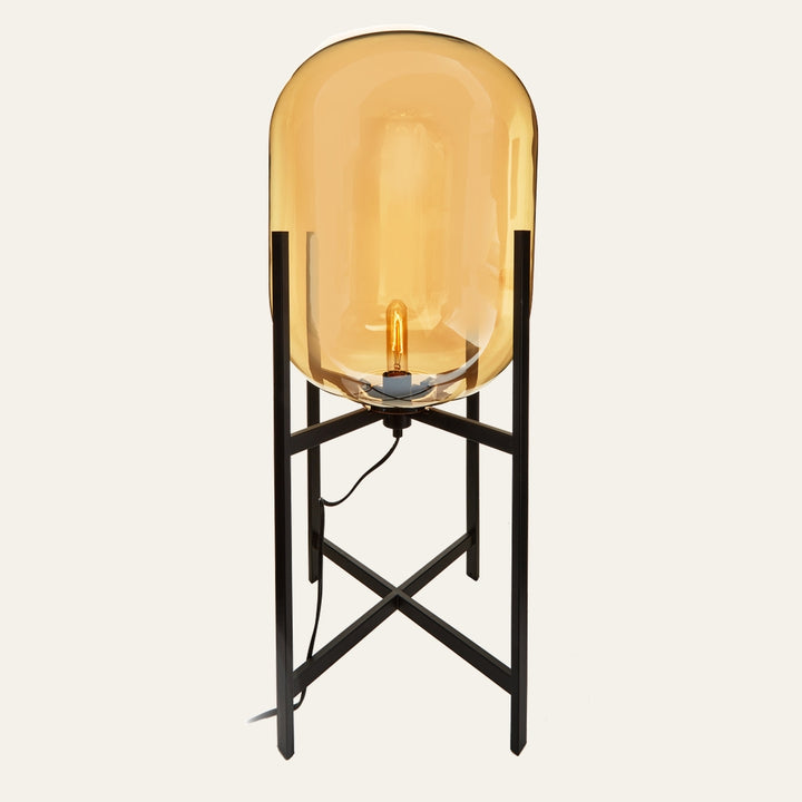 Erathia Glass Floor Lamp with tall amber glass oval shade, exposed filament bulb, and black metal cross-leg stand