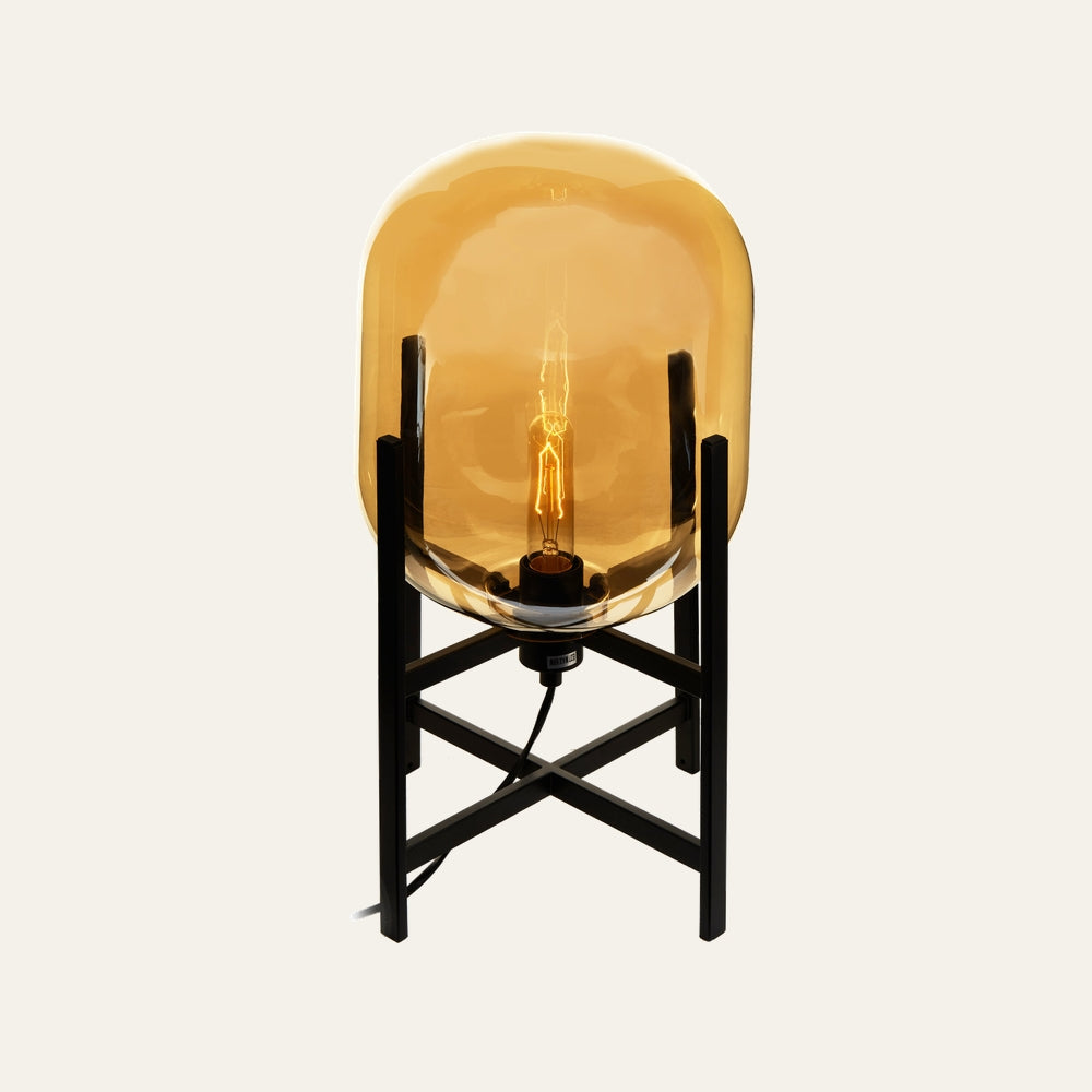 Erathia Glass Table Lamp with amber glass dome shade, visible filament bulb and black metal X-frame base