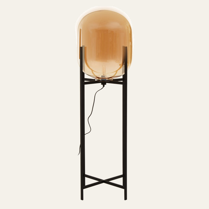 Erathia Large Floor Lamp with amber glass globe shade perched on a tall black metal stand with crossed base and visible power cord