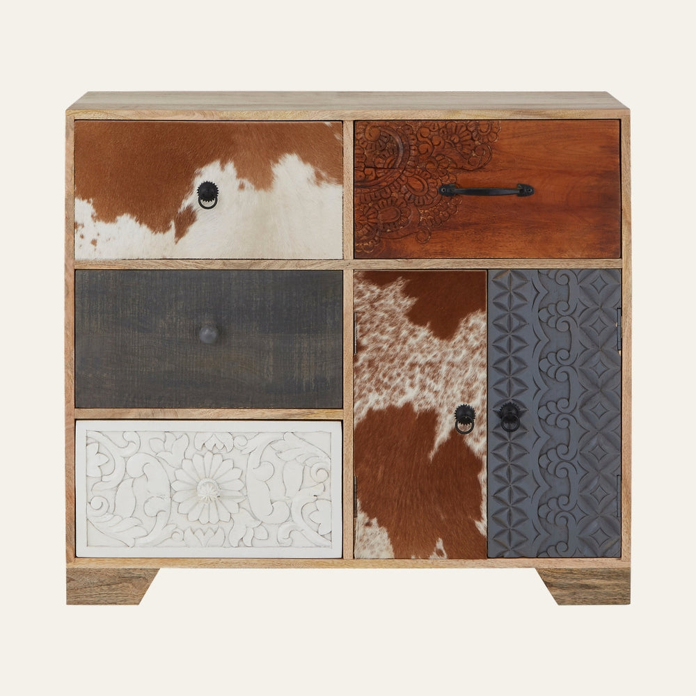 Esvora Tall Wood Sideboard with natural wood frame and patchwork of decorative panels – brown-and-white cowhide, carved white floral panel, dark gray carved panel, warm carved wood panel and black metal handles.