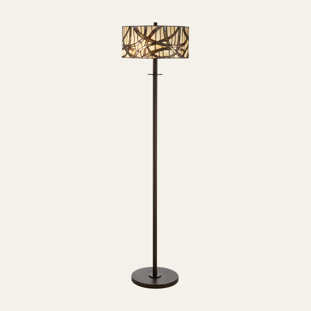 Evaya Floor Lamp with dark bronze metal pole and round base, drum stained-glass mosaic shade in cream, amber, and brown with abstract curved pattern.