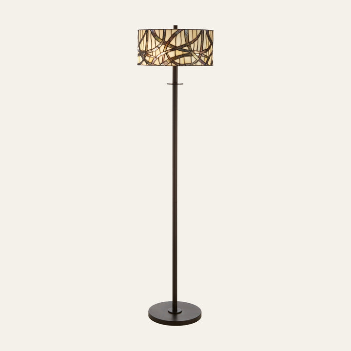 Evaya Floor Lamp with dark bronze metal pole and round base, drum stained-glass mosaic shade in cream, amber, and brown with abstract curved pattern.