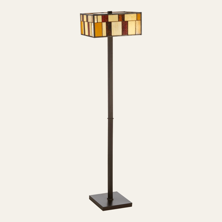 Evaya Floor Lamp with slim dark bronze metal pole and square base, topped by a rectangular stained-glass shade featuring amber, cream, and red geometric panels