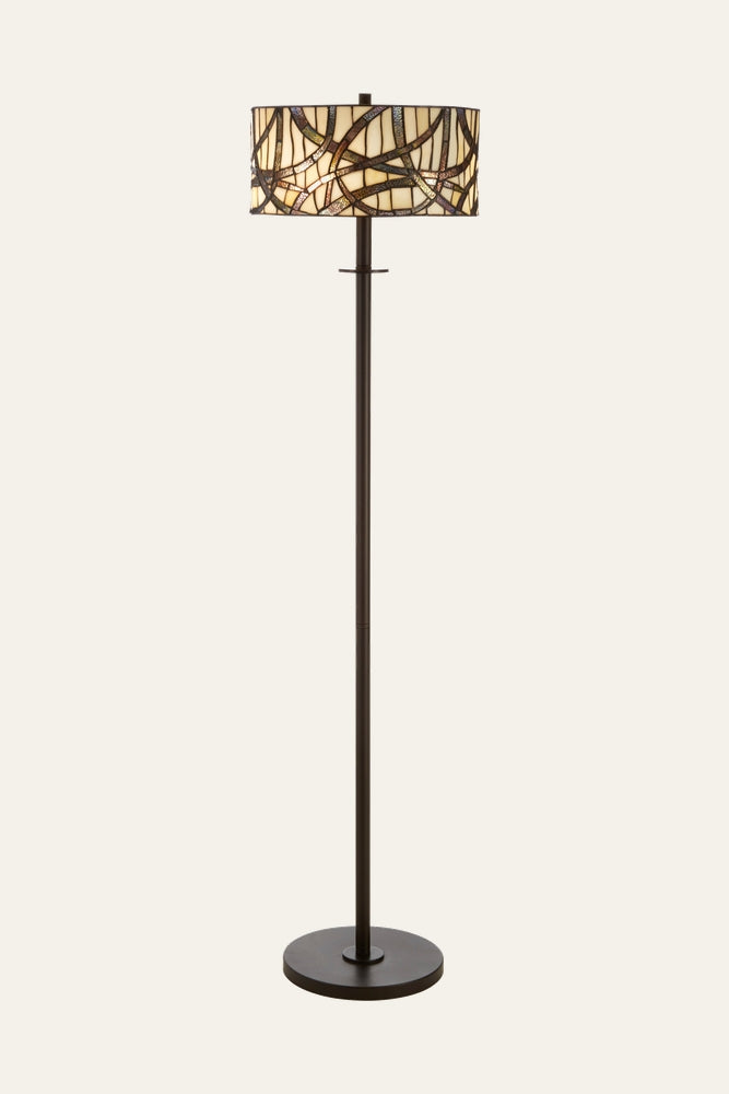 Evaya Floor Lamp with slender dark bronze metal pole and round base, topped by a drum stained-glass shade of cream and amber glass pieces in a brown leading mosaic pattern.