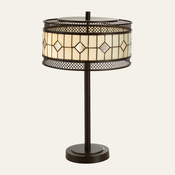 Evaya Table Lamp with dark bronze metal base and straight stem, round stained-glass drum shade with cream panels and textured diamond accents, and decorative mesh metal trim.