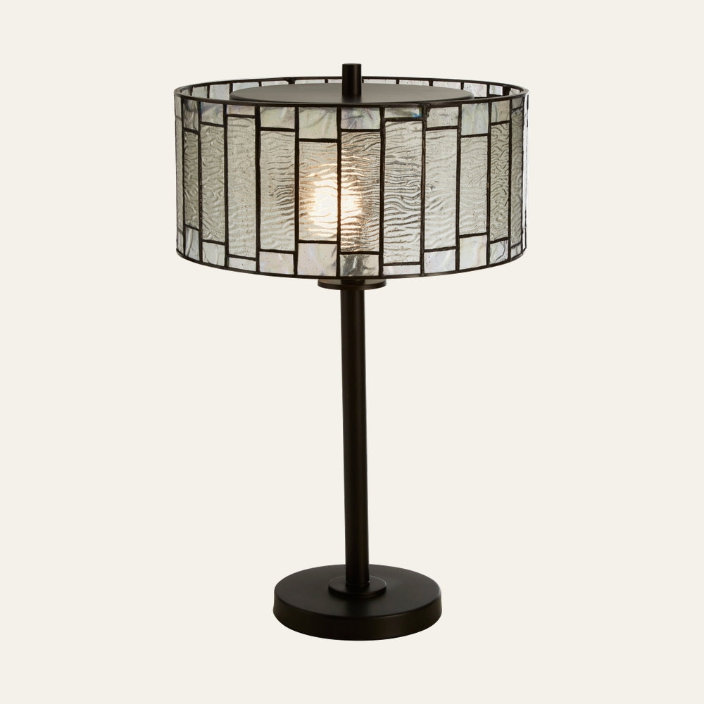 Evaya Table Lamp with dark metal round base and slender stem, lit drum Tiffany-style stained-glass shade of textured clear and iridescent rectangular panels with dark leaded lines
