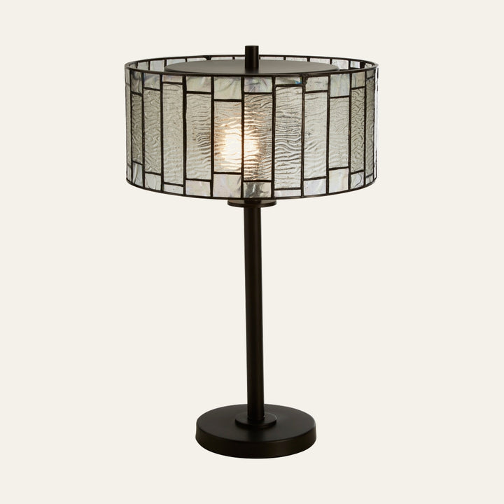 Evaya Table Lamp with dark metal round base and slender stem, lit drum Tiffany-style stained-glass shade of textured clear and iridescent rectangular panels with dark leaded lines
