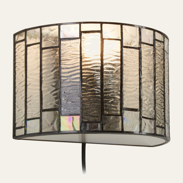 Evaya Wall Light — curved stained-glass wall sconce with vertical wavy-textured clear glass panels, iridescent accent squares and dark leaded metal framing, black cord visible