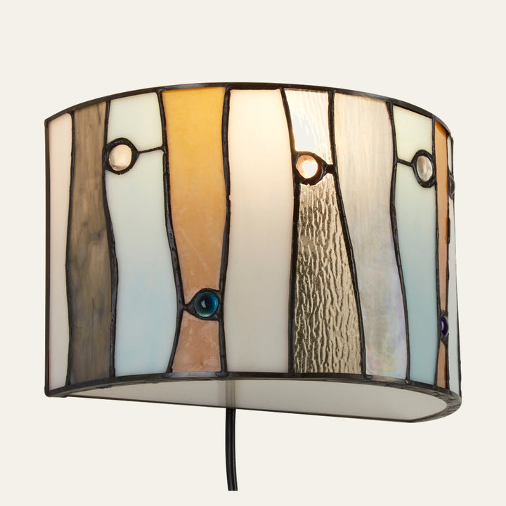 Evaya Wall Light — curved stained-glass shade with vertical multicolored panels edged in dark solder and small round glass jewels, white inner diffuser and visible black cord