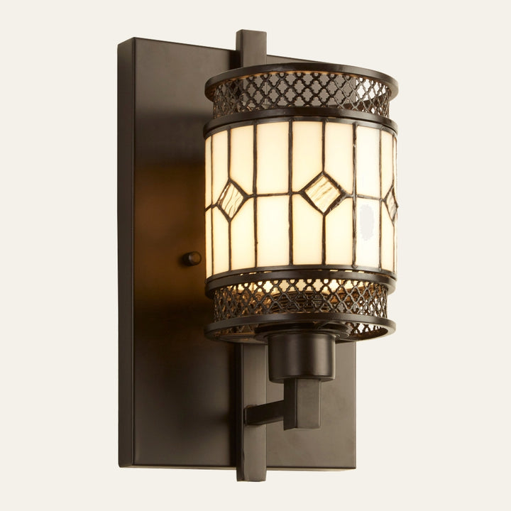 Evaya Wall Light with rectangular dark bronze metal backplate and cylindrical stained-glass shade featuring diamond-patterned panes and decorative bronze lattice trim, warm glowing light