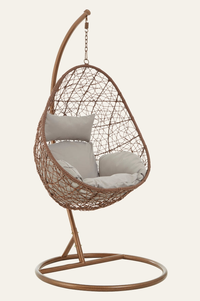 Evira Brown Rattan Hanging Chair with egg-shaped brown rattan weave, bronze metal stand with circular base, and light gray seat and back cushions