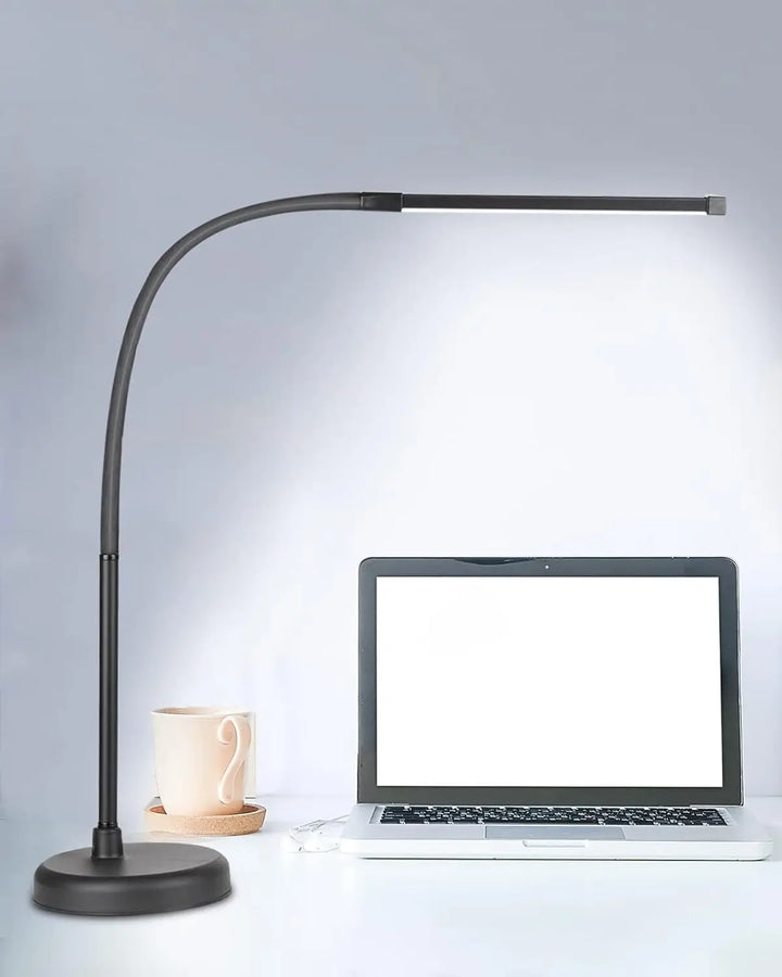 Black adjustable desk lamp next to a laptop on a light gray background