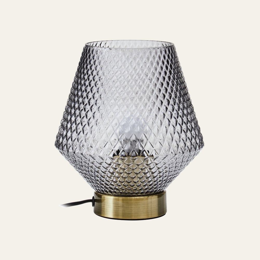 Lysara Table Lamp with diamond-patterned smoked glass shade, visible bulb inside and brushed brass cylindrical base with black power cord