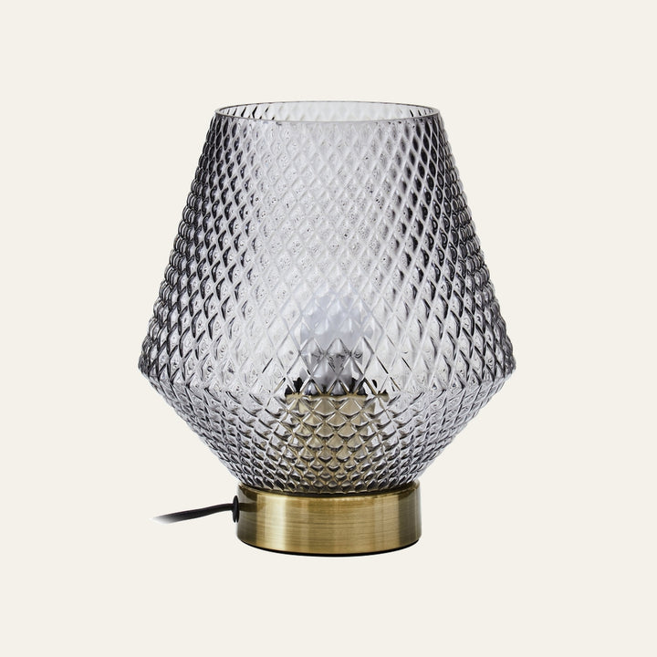 Lysara Table Lamp with diamond-patterned smoked glass shade, visible bulb inside and brushed brass cylindrical base with black power cord