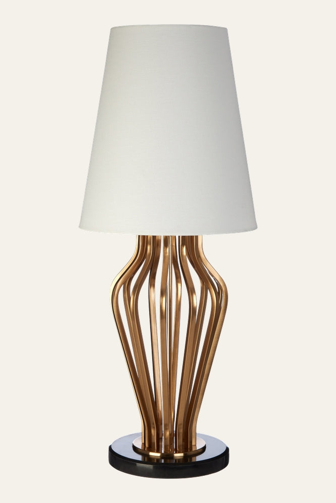 Nerdan Angular Table Lamp with white tapered fabric shade over a sculptural gold metal curved-rod base on a round black platform base