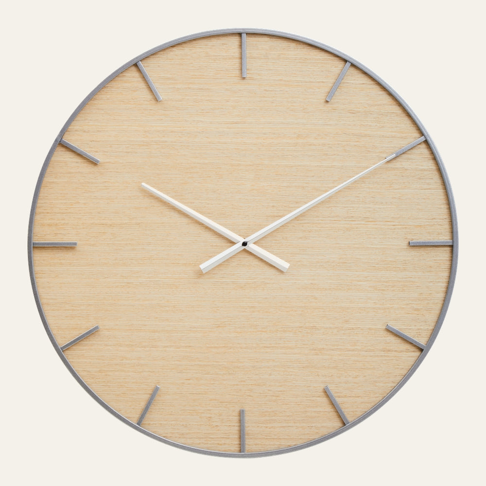 Rivor Wood Wall Clock with light oak wood face, slim white metal hands, and thin brushed silver hour markers and rim in a minimalist round design