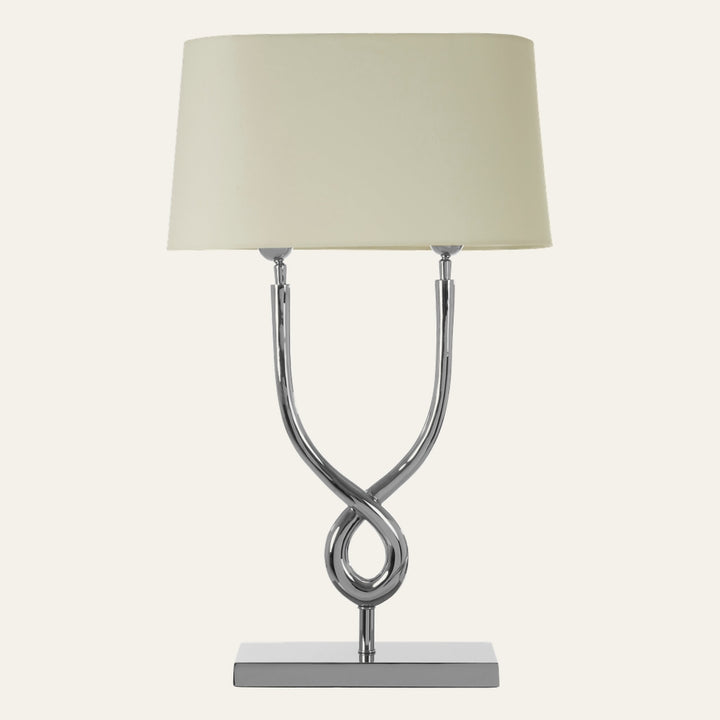 Selva Cross Base Table Lamp with polished chrome twisted cross base on a rectangular chrome platform and a cream fabric drum shade.