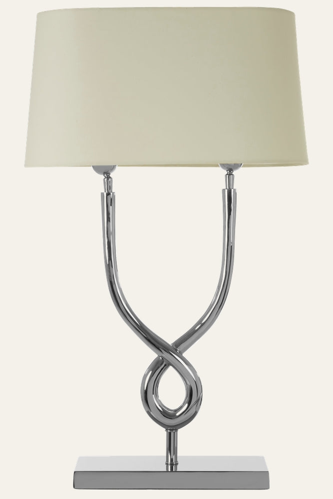 Selva Cross Base Table Lamp with cream fabric drum shade and twisted chrome cross base on a rectangular chrome plinth.