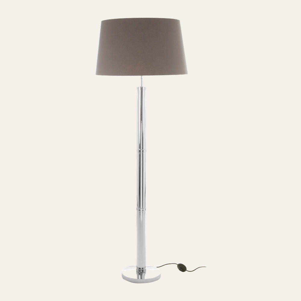Selva Tubular Base Floor Lamp with slender chrome tubular segmented base and round chrome pedestal, topped by a taupe fabric drum shade and an inline foot switch on the cord