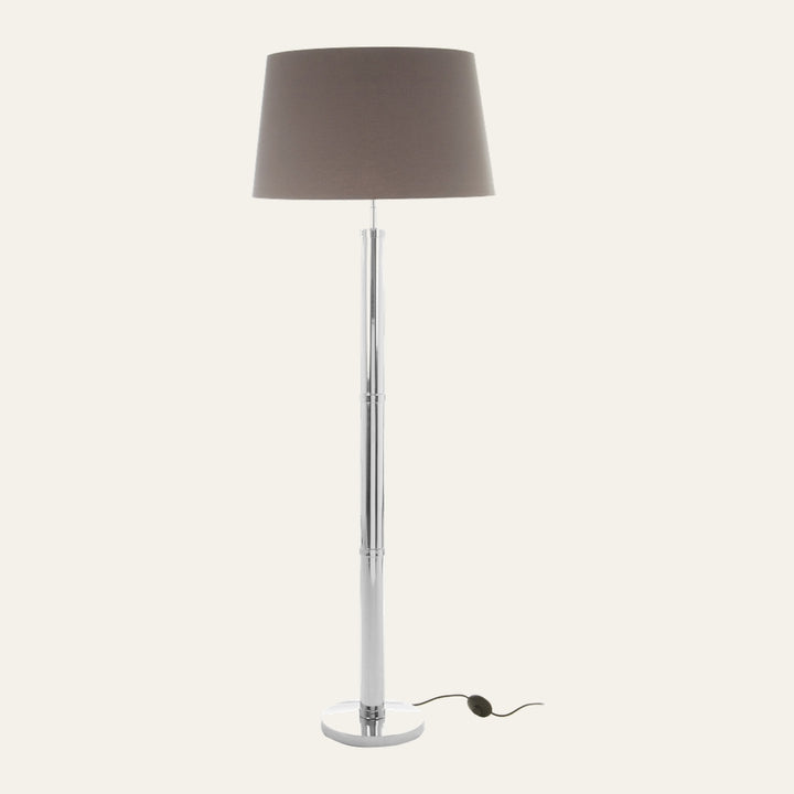 Selva Tubular Base Floor Lamp with slender chrome tubular segmented base and round chrome pedestal, topped by a taupe fabric drum shade and an inline foot switch on the cord