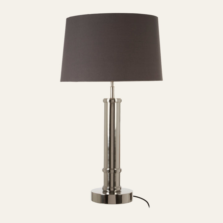 Selva Tubular Base Table Lamp with polished chrome tubular metal base on a round pedestal, dark gray fabric drum shade, and visible black power cord