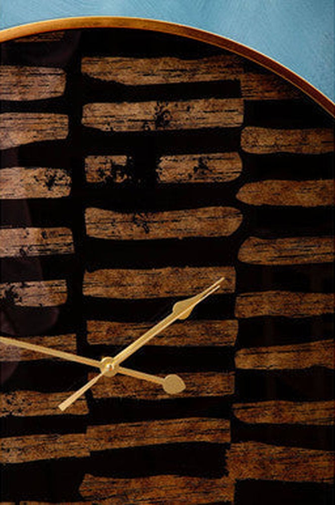 Soren Wall Clock close-up showing round wood-finish face with dark horizontal stripes, gold metal hands, and thin light-wood frame